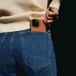 Coque iPhone 14 Mujjo en cuir fauve, partiellement glissée dans une poche de jean, avec découpe d’appareil photo surélevée