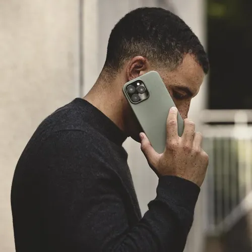 Coque en cuir Mujjo pour iPhone 16 Pro Max en vert fumé, présentée avec une personne tenant le téléphone à son oreille