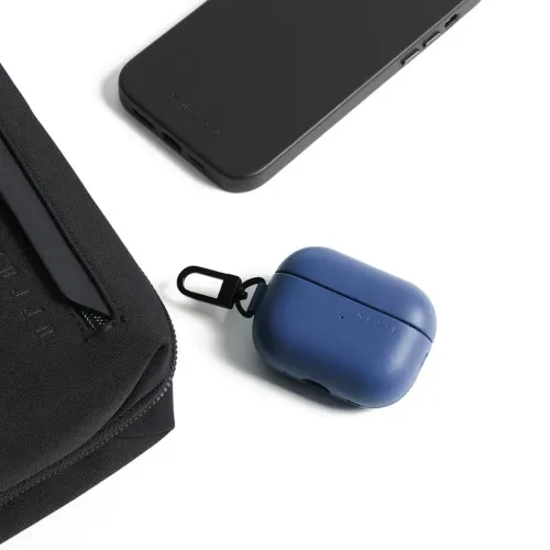 Mujjo blue leather AirPods Pro case with carabiner, front LED and hinges, on white background next to black mobile shell.