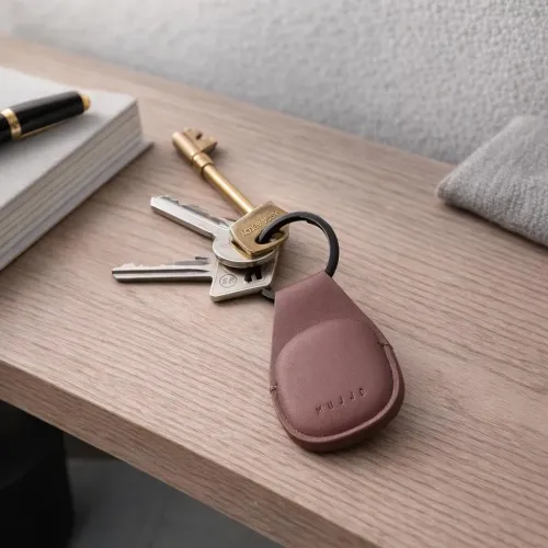 Mujjo Leather AirTag Keychain i brunt läder med fastsatta nycklar och präglad logotyp på en bordsskiva av trä